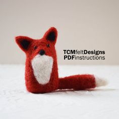 a red fox stuffed animal sitting on top of a white bed covered in snow next to the words tcm feltdesigns needle felted fox kit