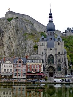 an old building with a steeple next to the water in front of a mountain