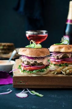 two hamburgers sitting on top of a cutting board next to a glass of wine