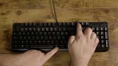 a person using a computer keyboard on a wooden table with their hands touching the keys