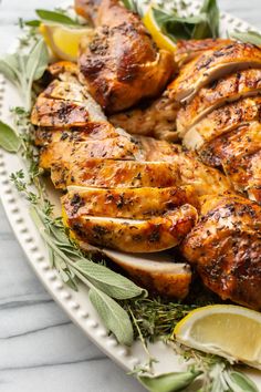 grilled chicken with herbs and lemons on a white platter