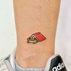 a small tattoo on the ankle of a woman's foot with a book and cup