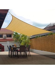 an outdoor dining area with table and chairs under a large yellow shade over the patio