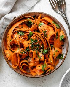 a bowl filled with pasta and sauce on top of a white table next to a fork