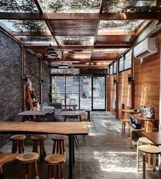 the inside of a restaurant with wooden tables and stools on concrete flooring, along with large windows