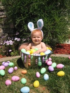 a baby sitting in an easter basket with eggs all over it and bunny ears on his head