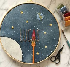 an embroidery project with scissors and thread on the table next to it is a space shuttle