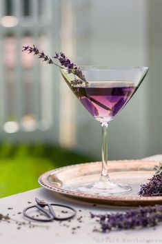 a glass filled with purple liquid sitting on top of a table next to a plate