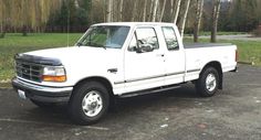 a white pick up truck parked in a parking lot next to some trees and grass