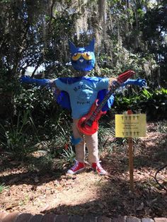 a person dressed in costume standing next to a sign with an electric guitar on it