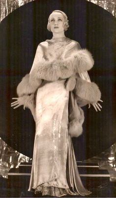 an old photo of a woman in a fur coat and dress with her hands on her hips