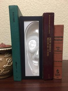 three books sitting on top of a wooden table next to a skull head in a box