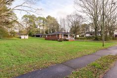 a small house in the middle of a grassy area with trees and houses behind it