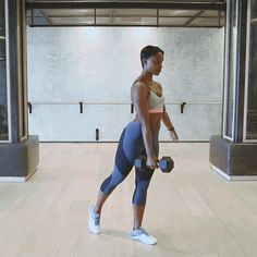 a woman holding a dumbbell while standing on a hard wood floor in an empty room