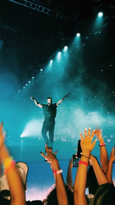 a man standing on top of a stage with his arms in the air while people are holding their hands up