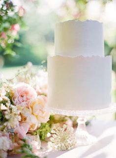 a white wedding cake sitting on top of a table next to pink and white flowers