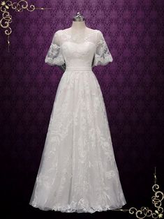 a white wedding dress on display in front of a purple wall with an ornate frame