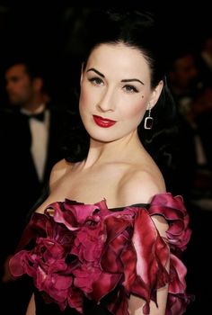 a woman in a red and black dress with large earrings on her left shoulder, posing for the camera