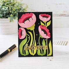 a card with pink flowers on it and the word bloom written in gold foil next to a pen