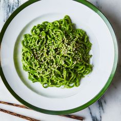 a white plate topped with green noodles next to chopsticks on a marble table