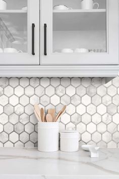 a kitchen counter with white cabinets and utensils in the center, on top of a marble tile backsplash