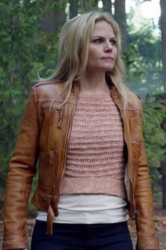 a woman standing in the woods wearing a brown leather jacket