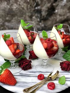 four desserts with strawberries and whipped cream on a marble platter next to gold utensils