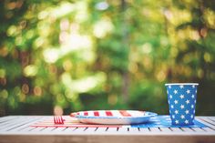 an american flag plate and cup sitting on a picnic table with trees in the background