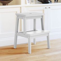 a white stool sitting on top of a hard wood floor next to a book shelf