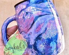 a hand holding a blue and purple coffee mug with glitter on it's side