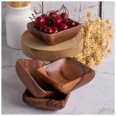 three wooden bowls with cherries in them are stacked on top of each other near dried flowers