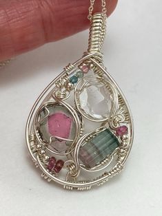 a hand holding a silver pendant with different colored stones