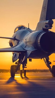 a fighter jet sitting on top of an airport tarmac at sunset with the sun behind it