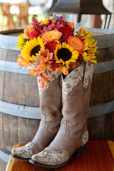 cowboy boots with sunflowers and other flowers in them sitting on top of a barrel