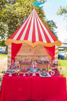 a red table topped with lots of desserts under a tent covered in white and yellow stripes