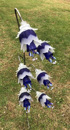 blue and white paper flowers are hanging from a metal pole in the grass on a sunny day