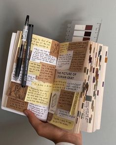 a hand holding an open book with many different types of papers and pens on it