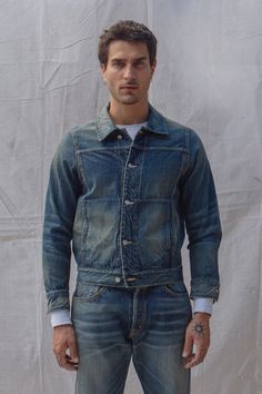 a man standing in front of a white backdrop wearing blue jeans and a jean jacket