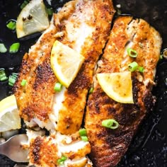 two pieces of fish with lemons and green onions in a skillet on a table