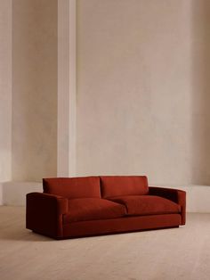 a red couch sitting on top of a hard wood floor next to a white wall