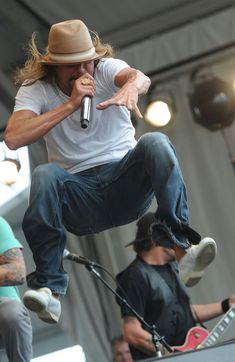 a man is jumping in the air with his guitar and singing into a microphone while other people watch