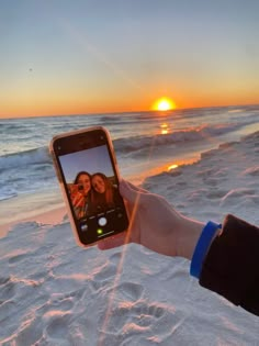 someone holding up their cell phone to take a selfie on the beach at sunset