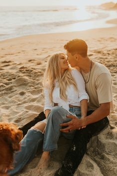 a man and woman kissing on the beach with a dog looking at each other in front of them