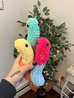 a person holding three crocheted items in front of a potted plant on the floor