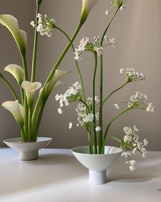 three white vases with flowers in them on a table