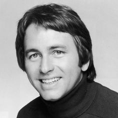 a black and white photo of a man in a turtle neck sweater smiling at the camera