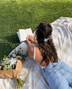 a woman sitting on the grass reading a book with flowers in front of her and an open book