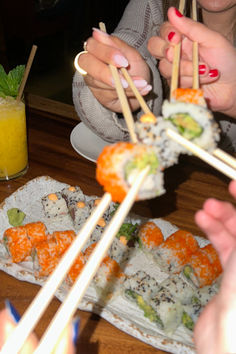 several people eating sushi with chopsticks at a table