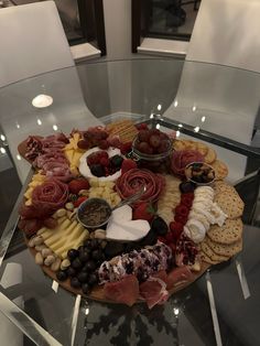 a platter with meats, cheeses and crackers on it sits on a glass table