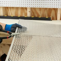 a person using a pair of scissors to cut metal grates on a piece of plywood